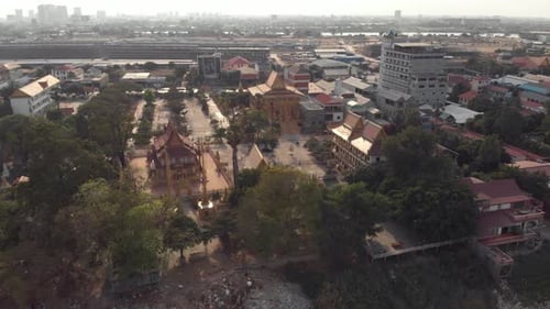 View from Mekong Riverbank to Golden Temple of Phnom Penh amidst cityscape - Aerial wide Fly-over sh