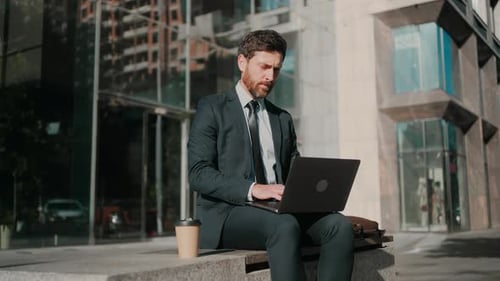 Man Works on Laptop Sitting Outside Office in Sunny Morning