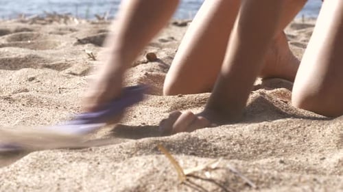 Close-up of kid’s arms and legs as it plays with spade on sand beach