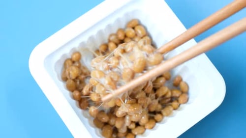 Wooden chopsticks holding Japanese natto beans on blue background top view.