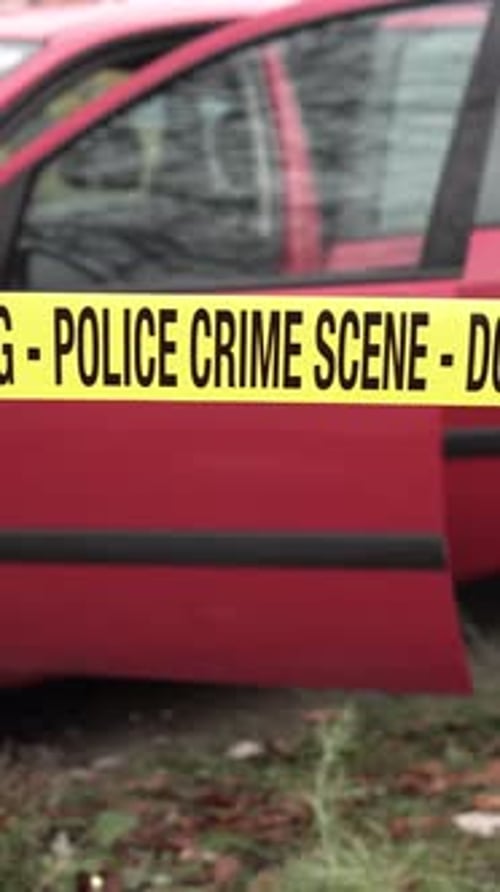 Vertical View of Police Crime Scene Tape in Front of Red Car With Open Doors, Close Up