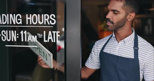 Open, sign and happy man at window of small business, coffee shop or start of service at restaurant