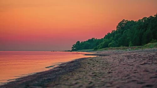Orange sunset sky reflects off the surface of a calm ocean at the beach - time lapse