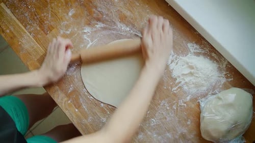 Hands Rolling Dough with Pin on Wooden Counter
