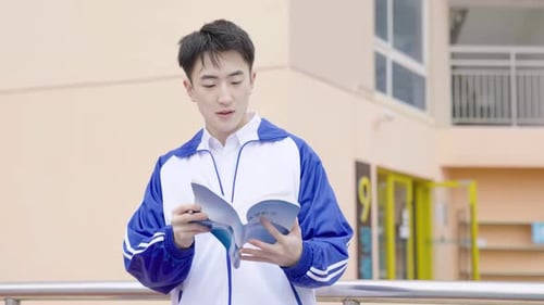 Handsome student reading book carefully turning pages exploring literature near contemporary library