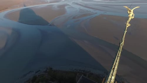 Drone flying near statue on spire of Mont Saint Michel abbey and view of bay. Aerial