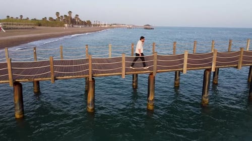 Young man walking on wooden pier at beach 4K