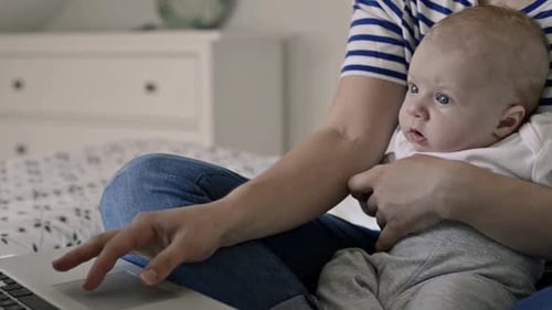 Mother holds infant while working on laptop