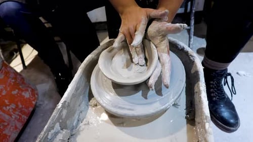 overhead close view of an African American hands spinning clay very sporadically while the mold begi