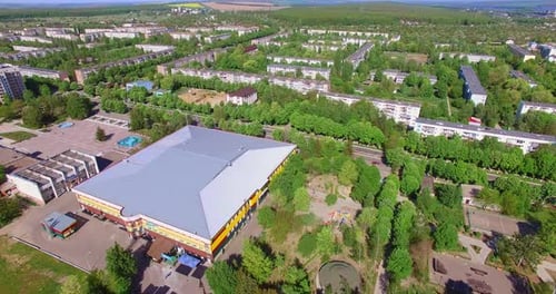 Large roof of a rectangular building in the city. Residential areas with lots of green trees.