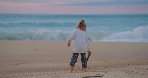 Ein kleines Mädchen im Sand zeichnet am Sandstrand bei Sonnenuntergang Nahaufnahme von hinten