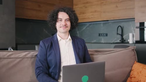 Curly Focused Business Man in a Jacket and Pajama Pants Working on Laptop Sitting at Home Office