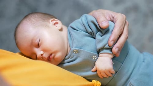 Newborn Sleeps Soundly With Adult Hand Resting On Chest