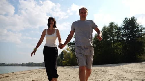 Couple Holding Hands Walks on Beach on Sunny Day
