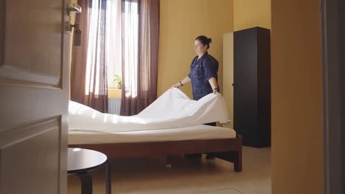 Female Housekeeper Changing Bedding in a Hotel Room