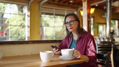 Woman is Using Smartphone and Drinking Coffee in the Cafe Slow Motion