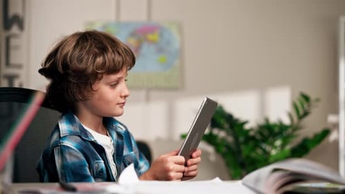 in the Children's Room a Schoolboy in a White Sweater and a Blue Checkered Shirt at a Desk Does