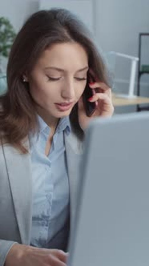 Close Up Face Young Businesswoman Speaks on Phone Working on Laptop Computer On Background People