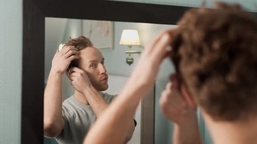 Man Combing Hair in Front of Bathroom Mirror