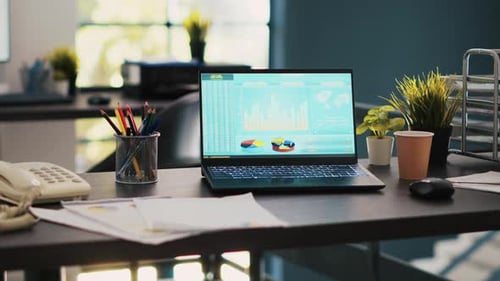 Empty Desk with Laptop Displaying Data Charts