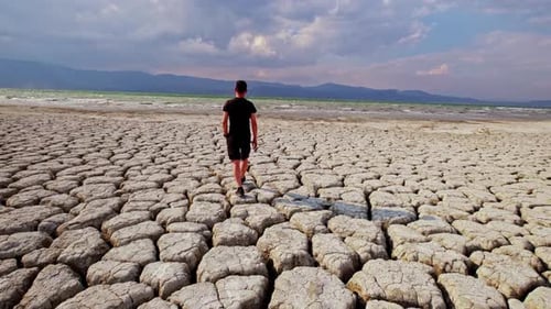 Man Walks on Cracked Earth Near Body of Water