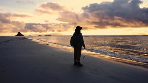 Silhouette of a Girl in a Hat with a Backpack at Sunset Near the Beach By the Ocean