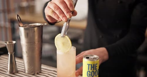 Hands, tongs and bartender with lemon slice in cocktail for drink preparation closeup in pub