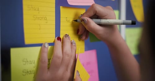 La main d'une femme écrit un message sur une note collée sur une vitre.