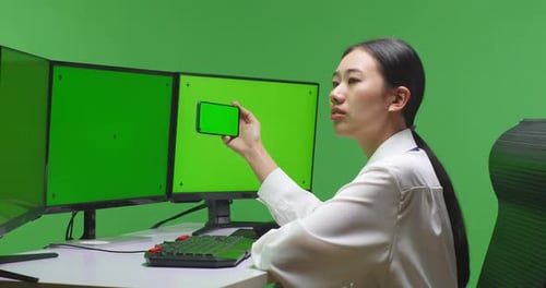 Asian Man Using Mobile Phone And Multiple Monitor With Mock Up Green Screen In Green Screen Studio