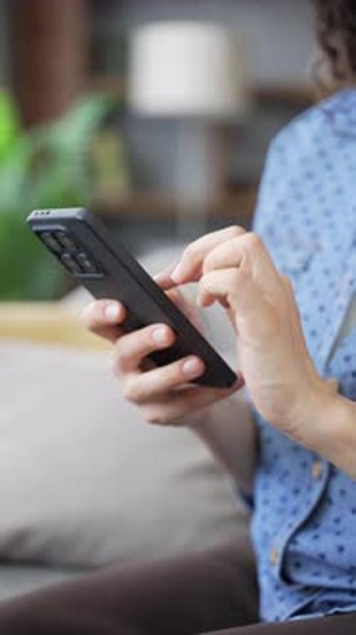 Close up of female hands using mobile phone in living room. Young woman engaged in digital