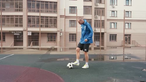 Young Man Practices Soccer Skills on Wet Urban Court