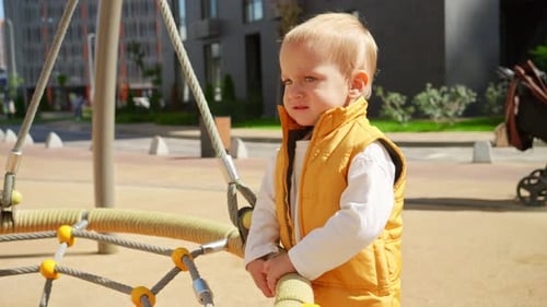 Upset crying baby boy standing on the playground at swing