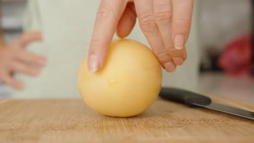 Une femme fait tourner des fruits de pépino sur une planche à découper, en examinant de quel côté couper.