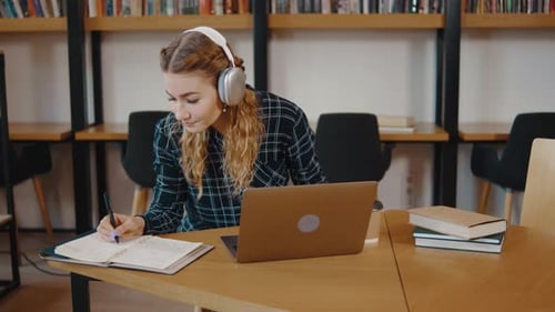 Jeune fille, étudiante, assise à son bureau, utilise un PC portable, un ordinateur portable, regarde à distance, apprentissage en ligne