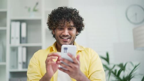 Cheery freelancer employee entrepreneur man celebrate online victory sit at office holds cellphone c