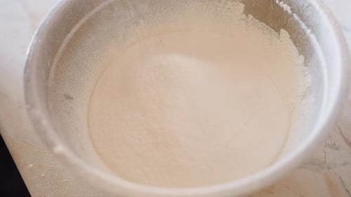 Mehl wird während der Backzubereitung in eine Edelstahlschüssel gesiebt