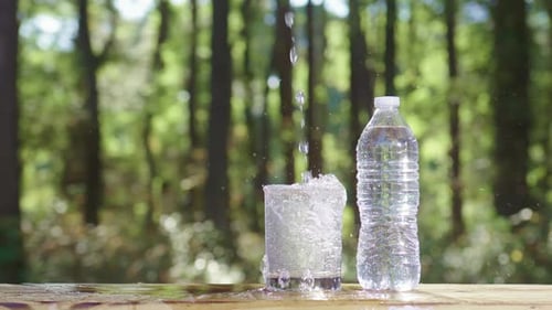 Klare Wasserblasen und spritzendes Süßwasser im Glas mit naturverwischtem Trinkwasser im ruhigen Wald