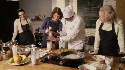 Un chef aide un participant à utiliser un mixeur pendant un cours de cuisine