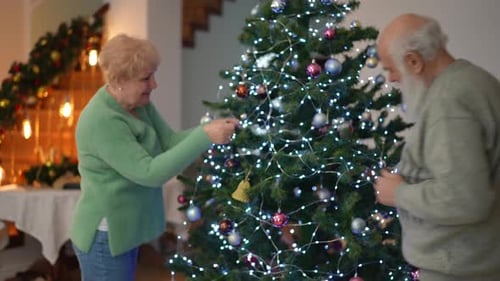 Senior Couple Decorates Christmas Tree Together Indoors