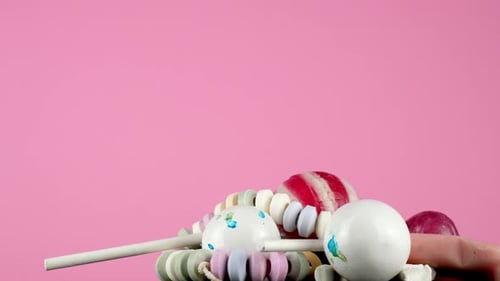 A portion of delicious assorted candy, rotating on a platter against a bright baby-pink studio backg