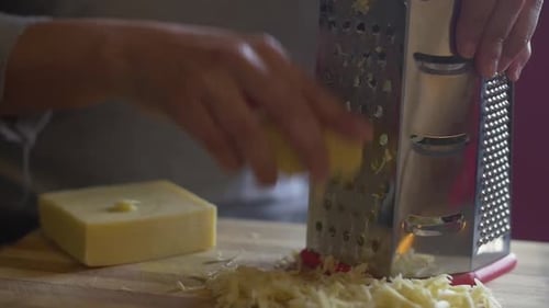 Woman's hand grating cheese onto a wooden chopping board. Slow Motion