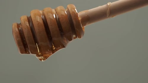 Honey is dripping from a wooden honey spoon. Honey spoon on a gray background. Close-up.
