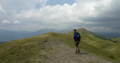 Aerial shot of a carefree man tourist with backpack is hiking on the path in the middle of hills s