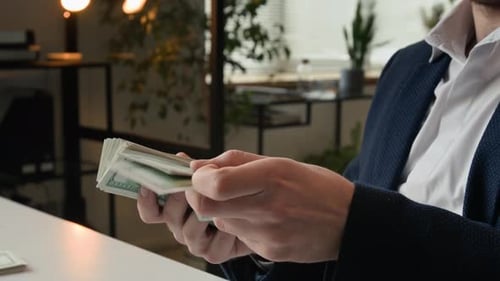 Hände eines erfolgreichen Geschäftsmannes, der am Schreibtisch einen Stapel Dollarscheine in der Hand hält