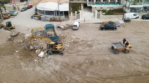 Orbiting aerial view of excavator filling up a dump truck on a sandy beach during winter time