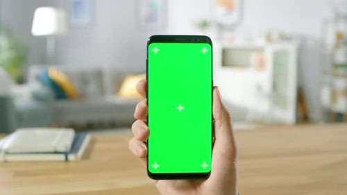 Close-up of a Man Holding Modern Green Mock-up Screen Smartphone and Making Touchscreen Gestures. T