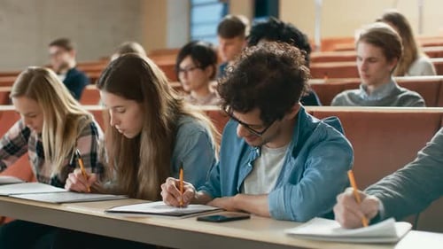 Grupo multiétnico de estudiantes que escriben después de que el profesor comience a reír. Los jóvenes brillantes tienen