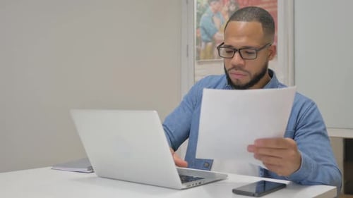 Happy Young Adult Looking at Document at Desk