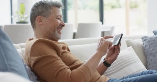 Happy Man Using a Smartphone While Relaxing on a Sofa at Home