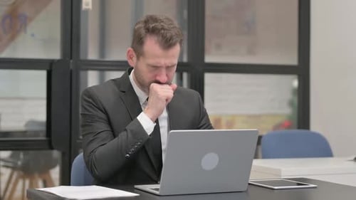 Man Coughing While Working at Office Laptop
